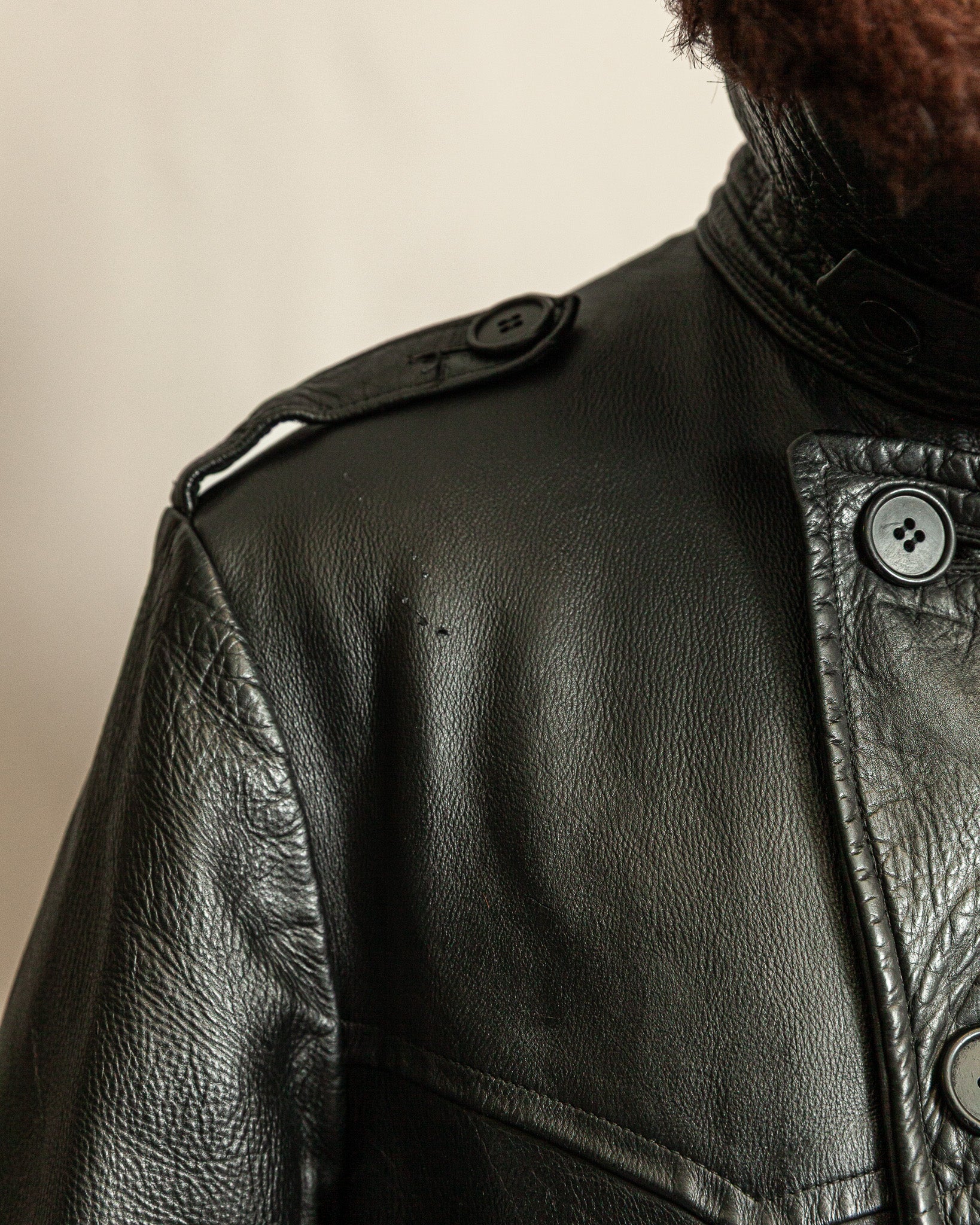 Close-up of a black leather jacket with buttons on a beige background
