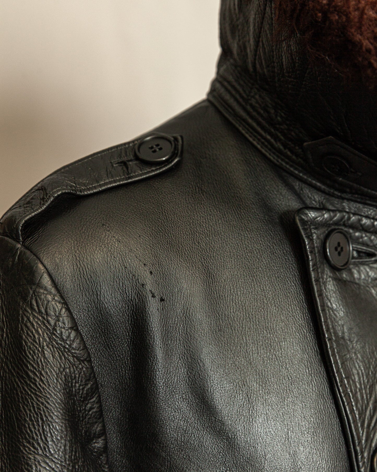 Close-up of a black leather jacket with buttons on a neutral background