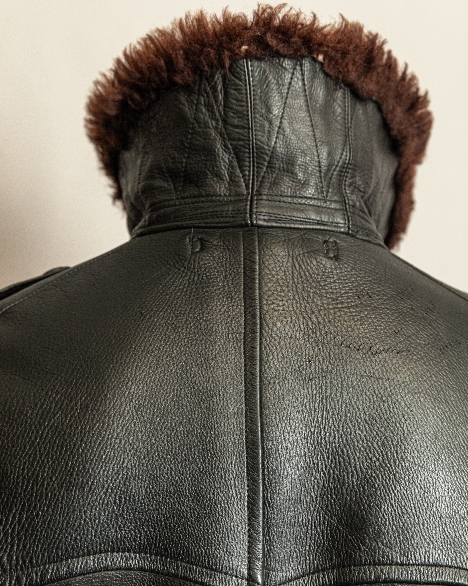 Close-up of a black leather jacket with brown fur lining on a beige background