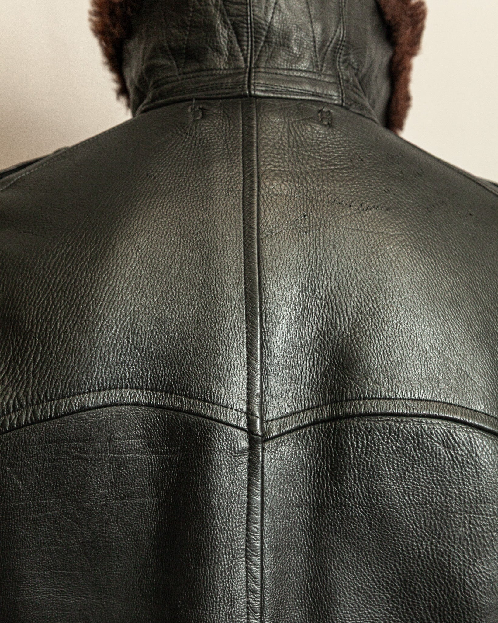 Close-up of a black leather jacket with fur lining on a neutral background