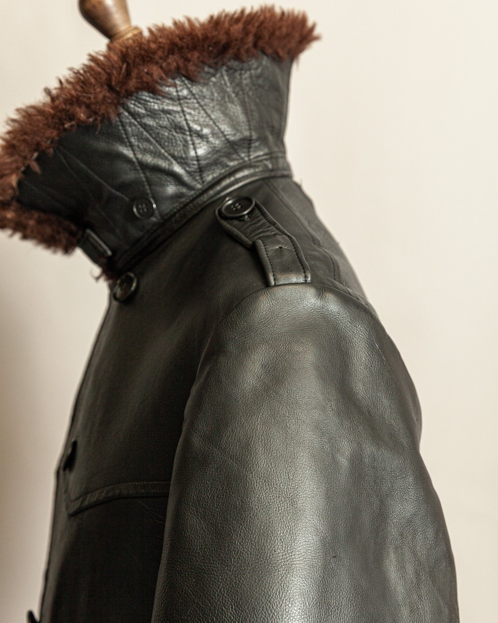 Black leather jacket with brown fur hood on a neutral background