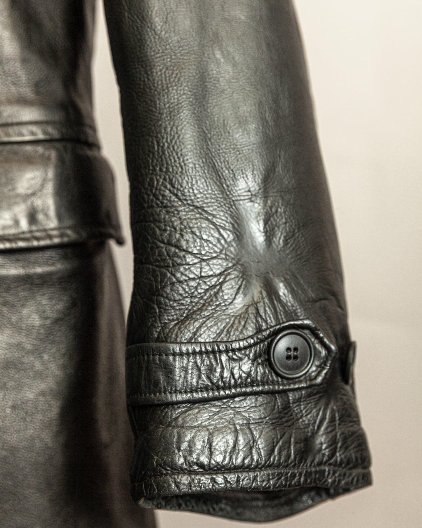 Close-up of a black leather sleeve with a button on a beige background