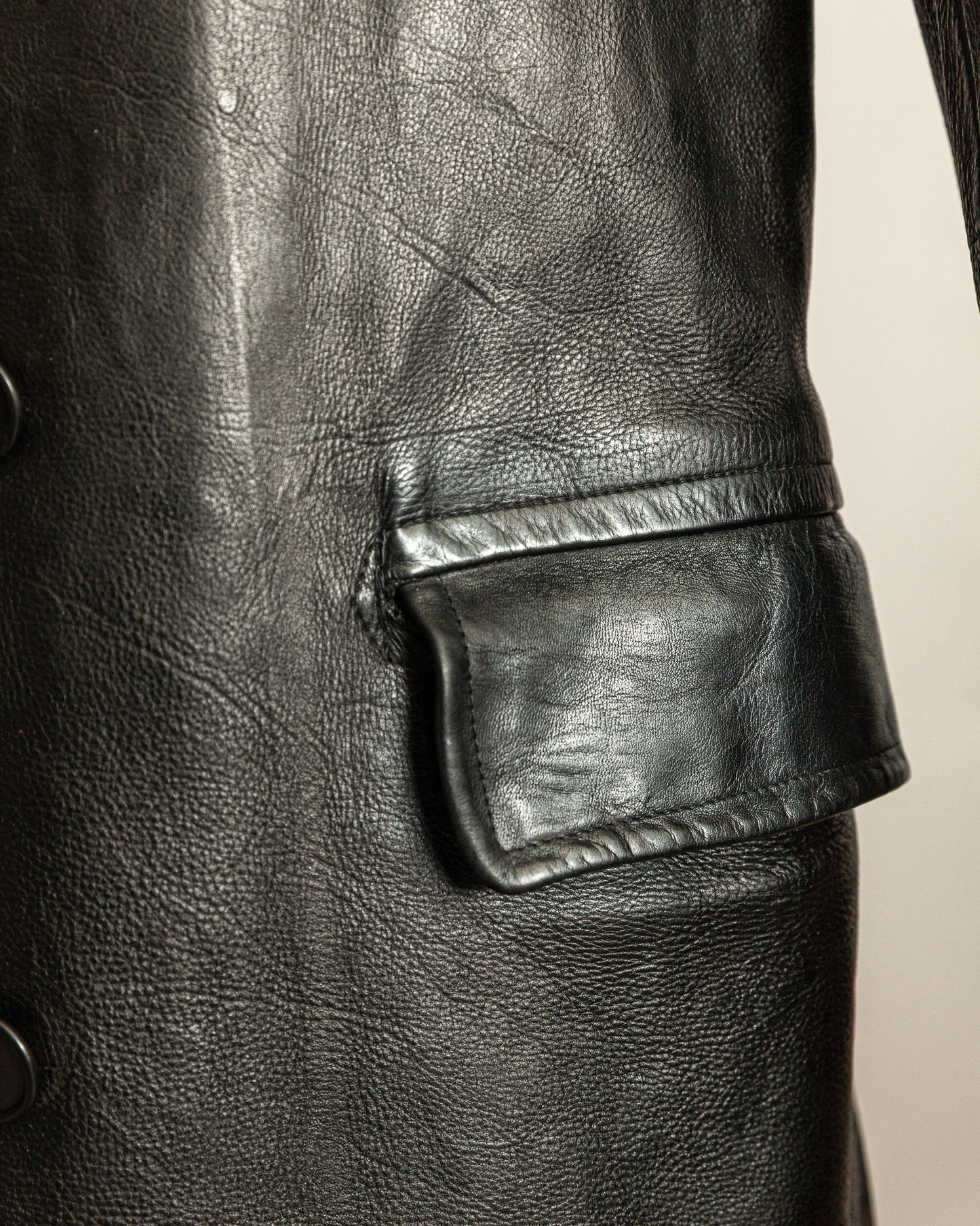 Close-up of a black leather jacket with a pocket detail on a beige background
