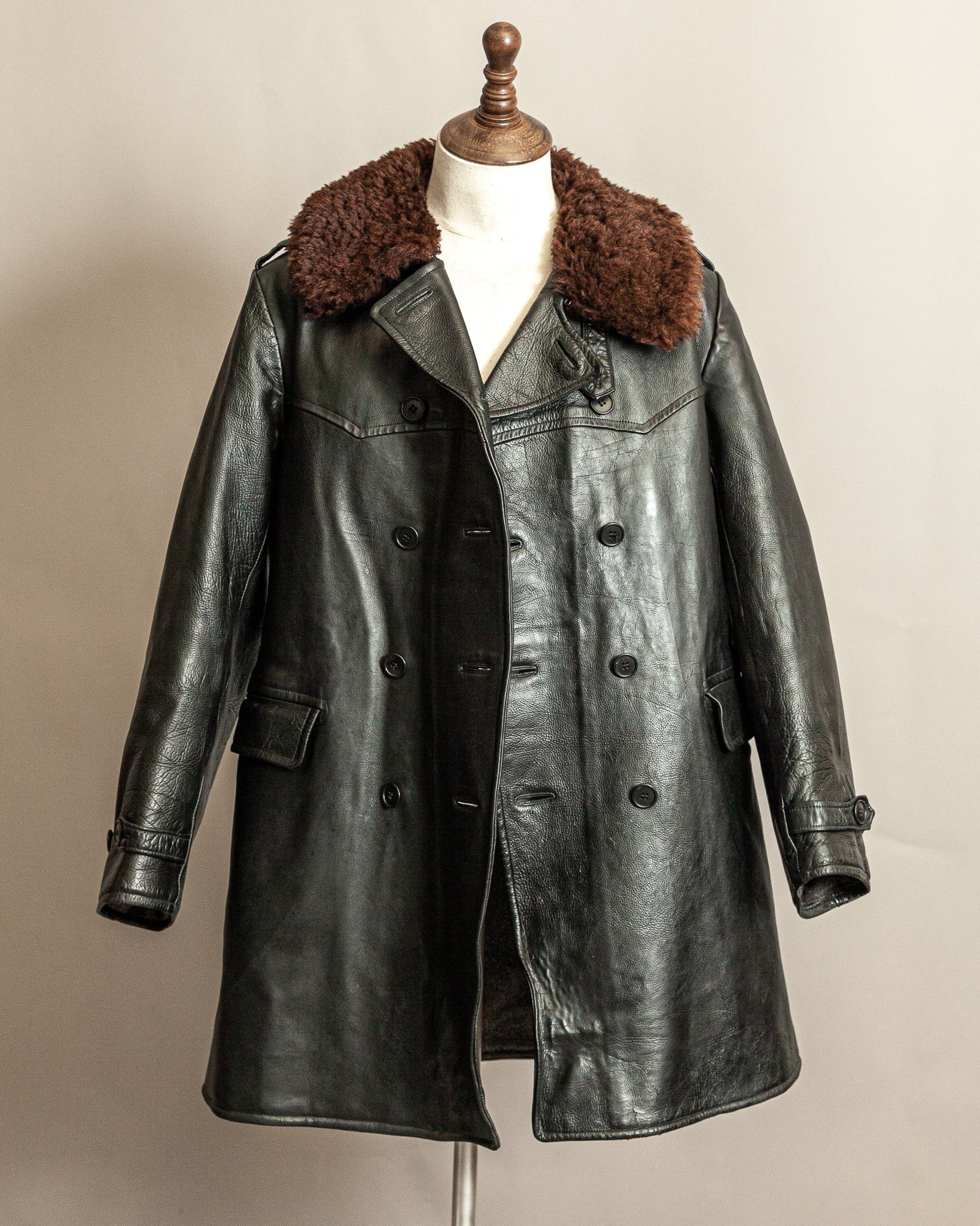 Vintage Swedish WW2 1940s Black Goatskin leather long army trench coat with real wool collar on a mannequin, the buttons are unfastened and is open, this is poised against a beige background