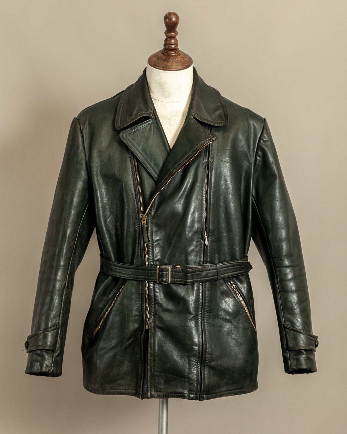 Vintage 1950s German Haelson green leather dispatch rider jacket displayed on a mannequin with belt and asymmetrical zip front.