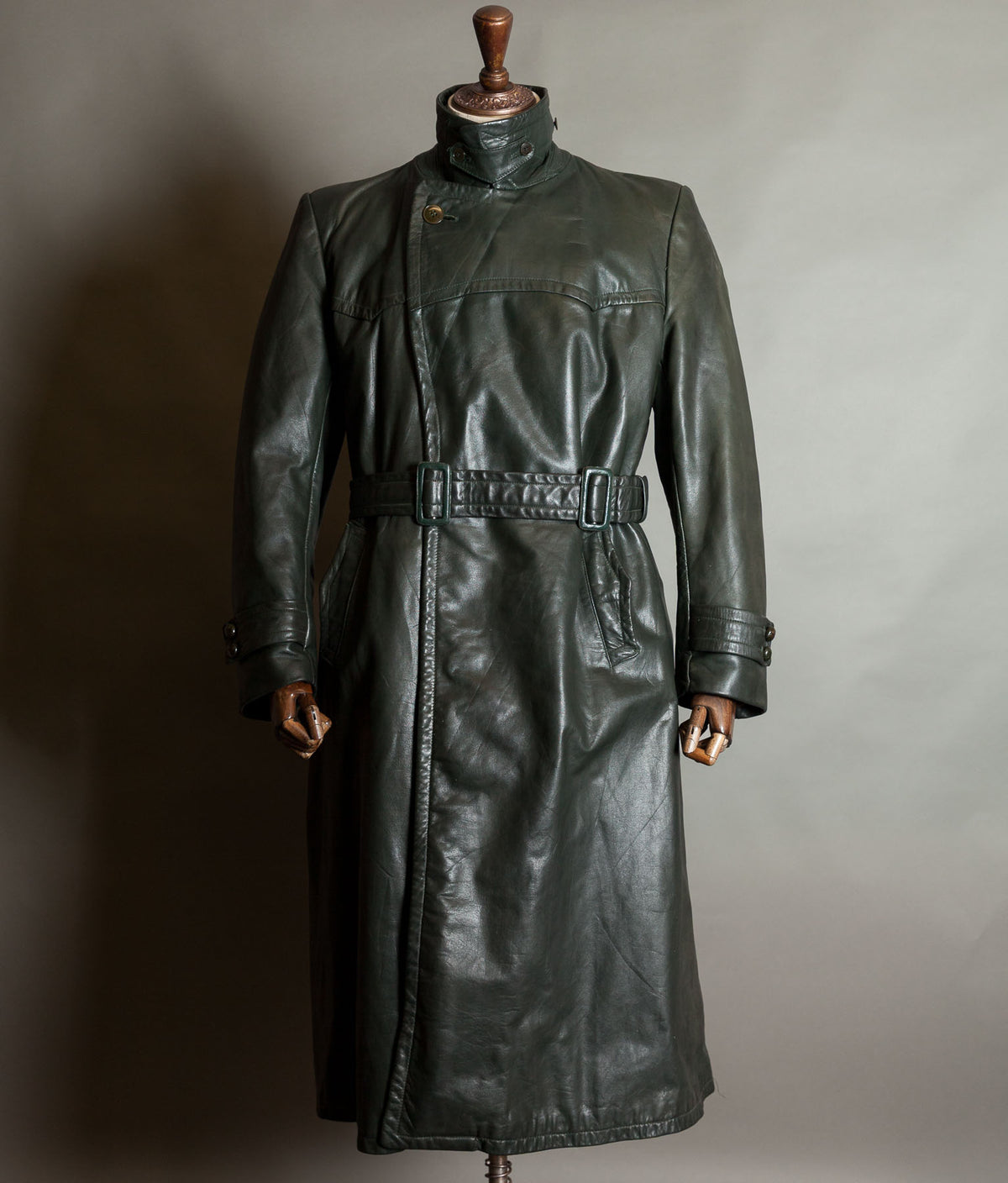 Original WW2 German leather trench coat with high buttoned collar and twin-buckle belt, displayed on a wooden mannequin